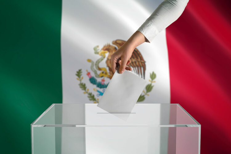 una mujer deposita su voto en una urna con la bandera de México de fondo