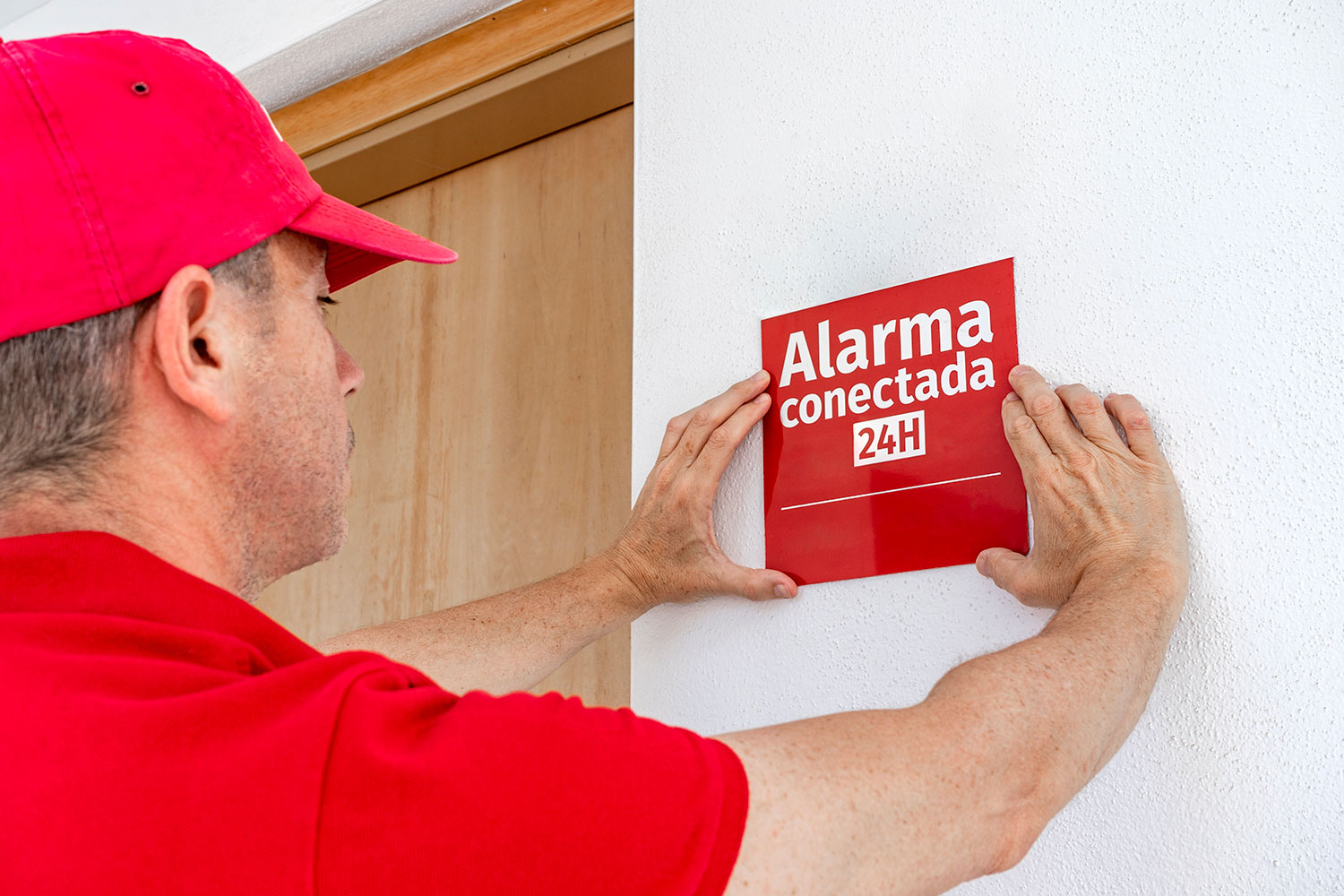 un hombre coloca el cartel de Alarma Conectada 24 horas en la entrada de una vivienda