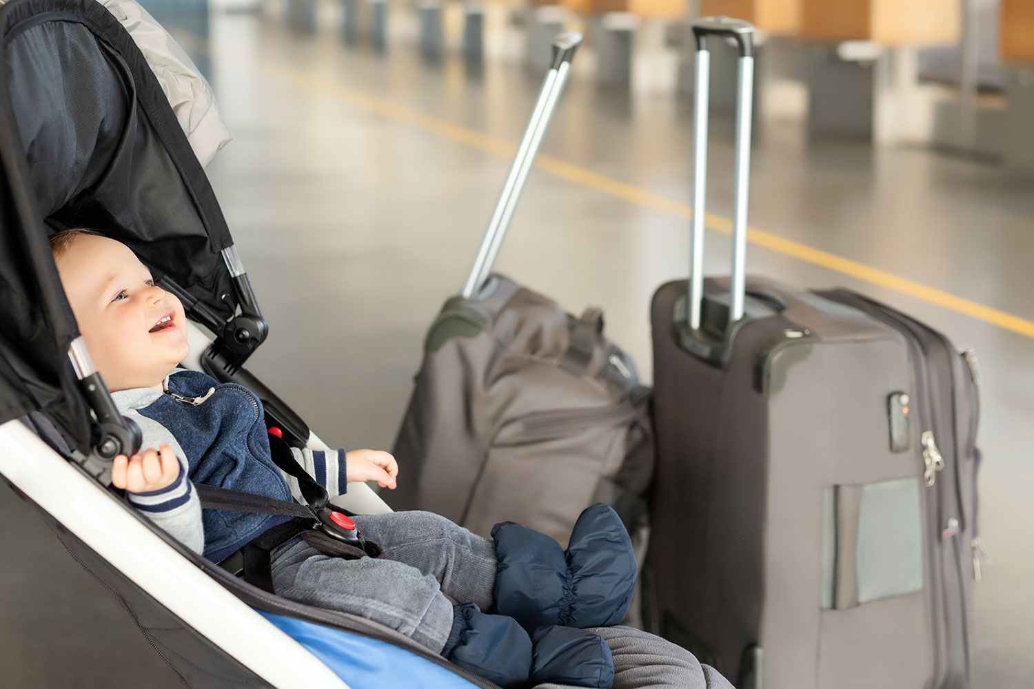 un bebé en su carrito junto a dos maletas de viaje en el aeropuerto