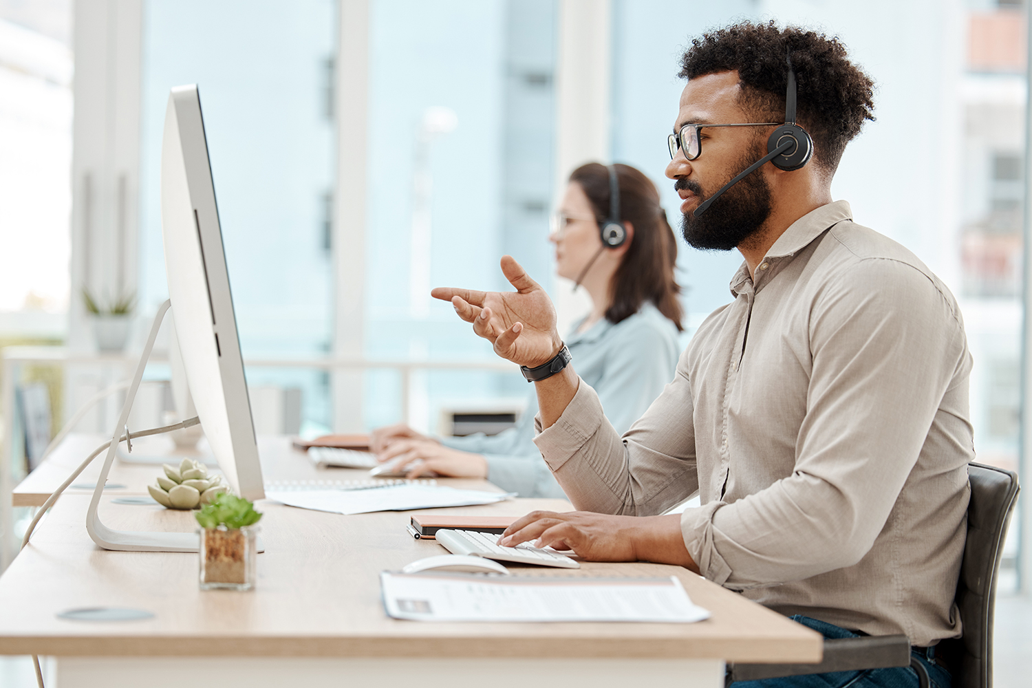 dos personas trabajan con sus ordenadores y auriculares en un servicio de soporte técnico